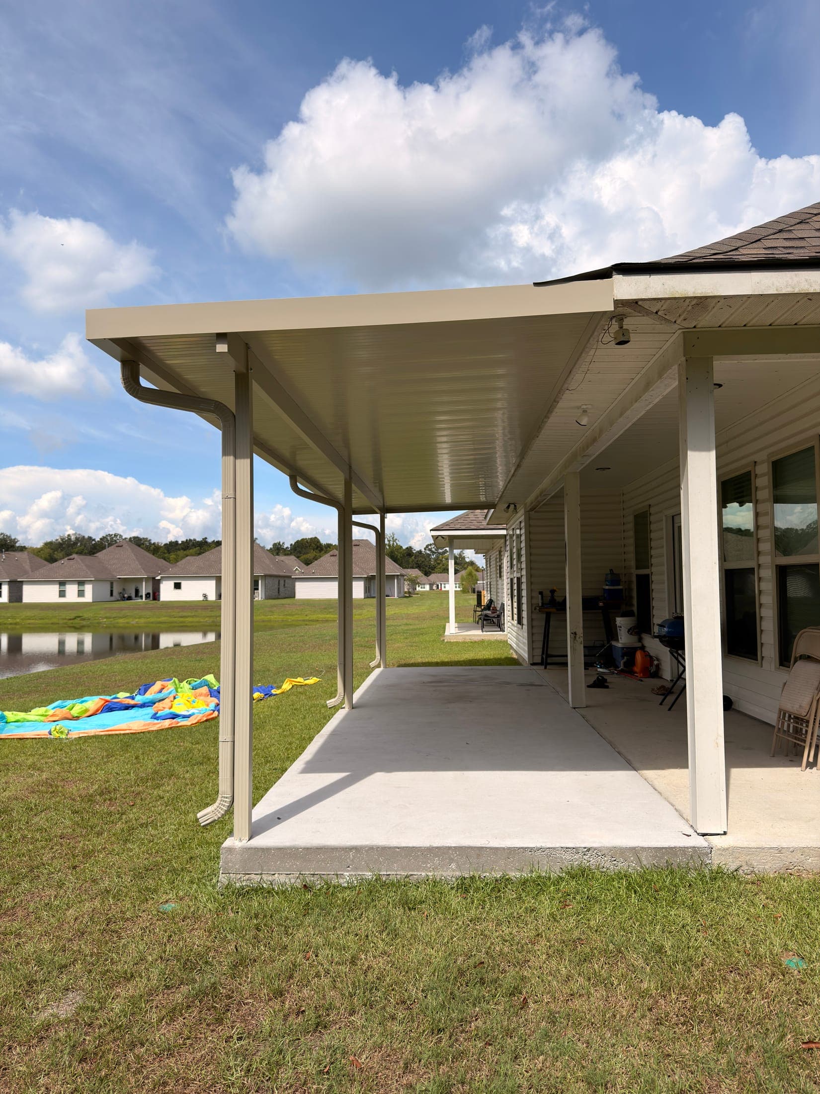 Long tan aluminum patio cover on slim posts across the back of a home
