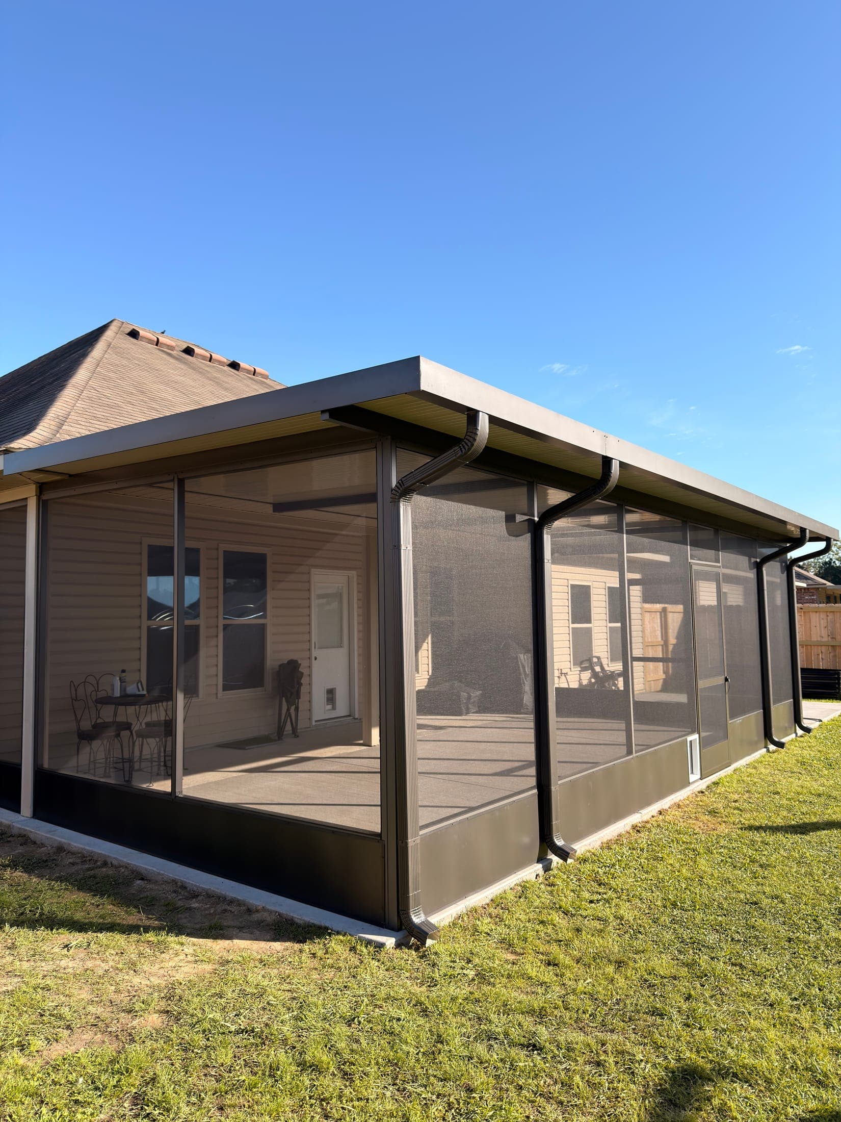 Screened patio enclosure with a dark aluminum frame across the back of a brick home