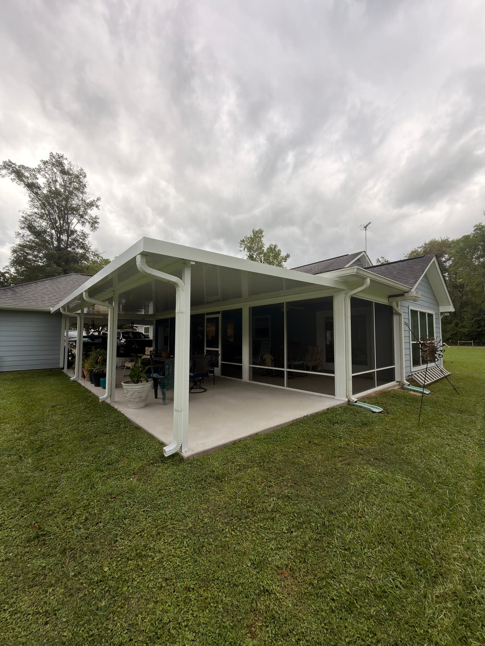White patio cover beside a screened room over a concrete patio, seen from the lawn