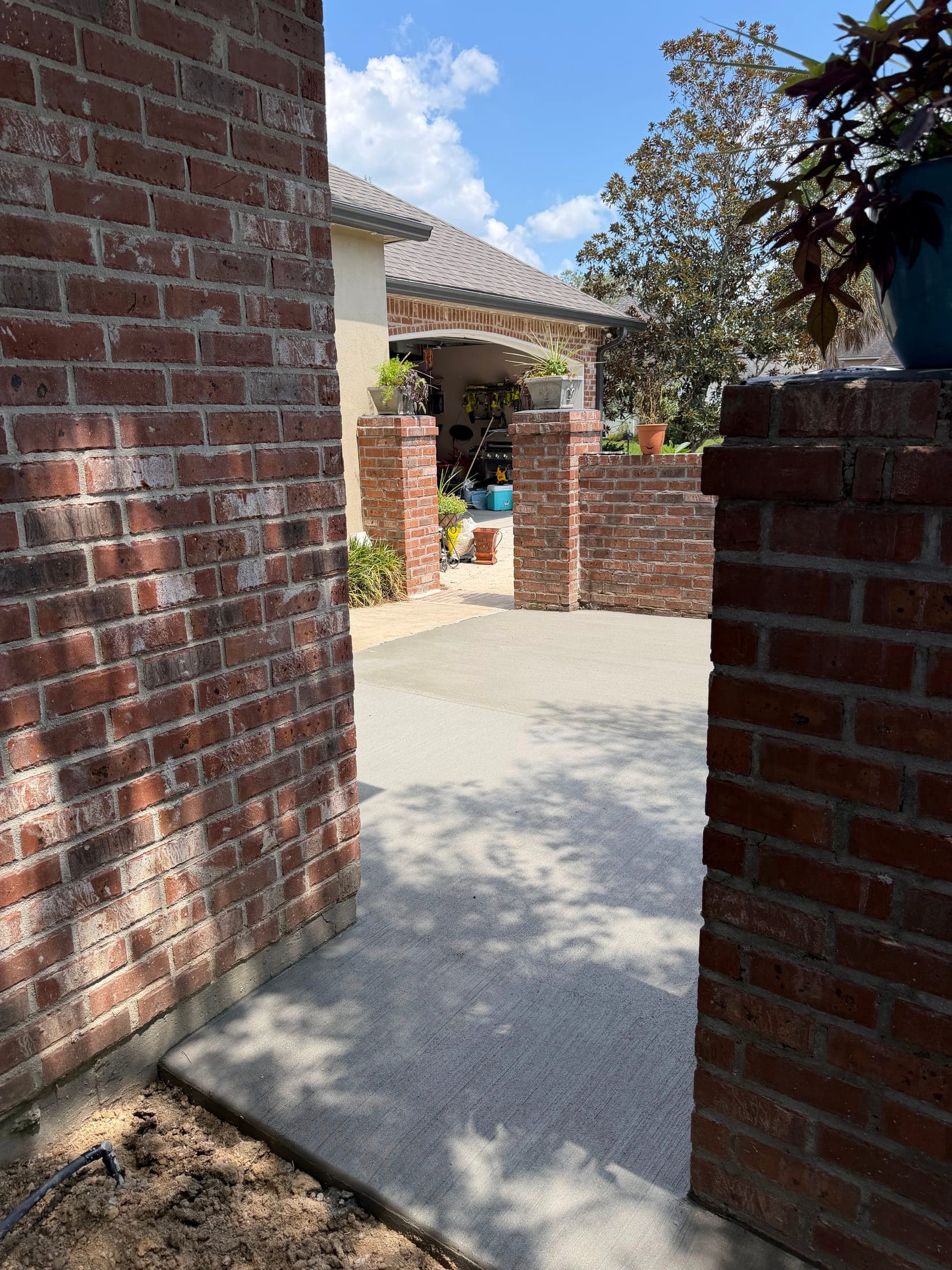 Broom-finished concrete walk between two brick columns leading toward a brick home's courtyard