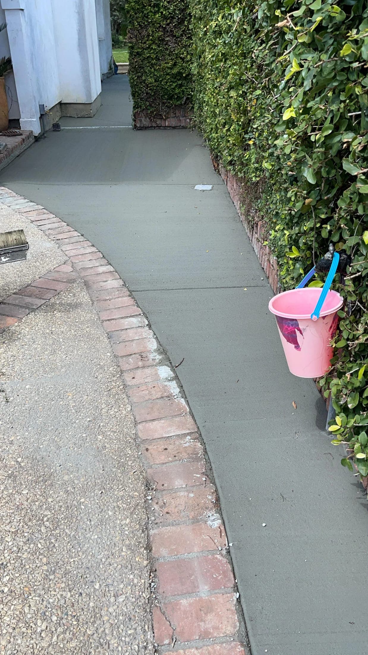 Fresh concrete walkway curving along a brick edge and a trimmed hedge