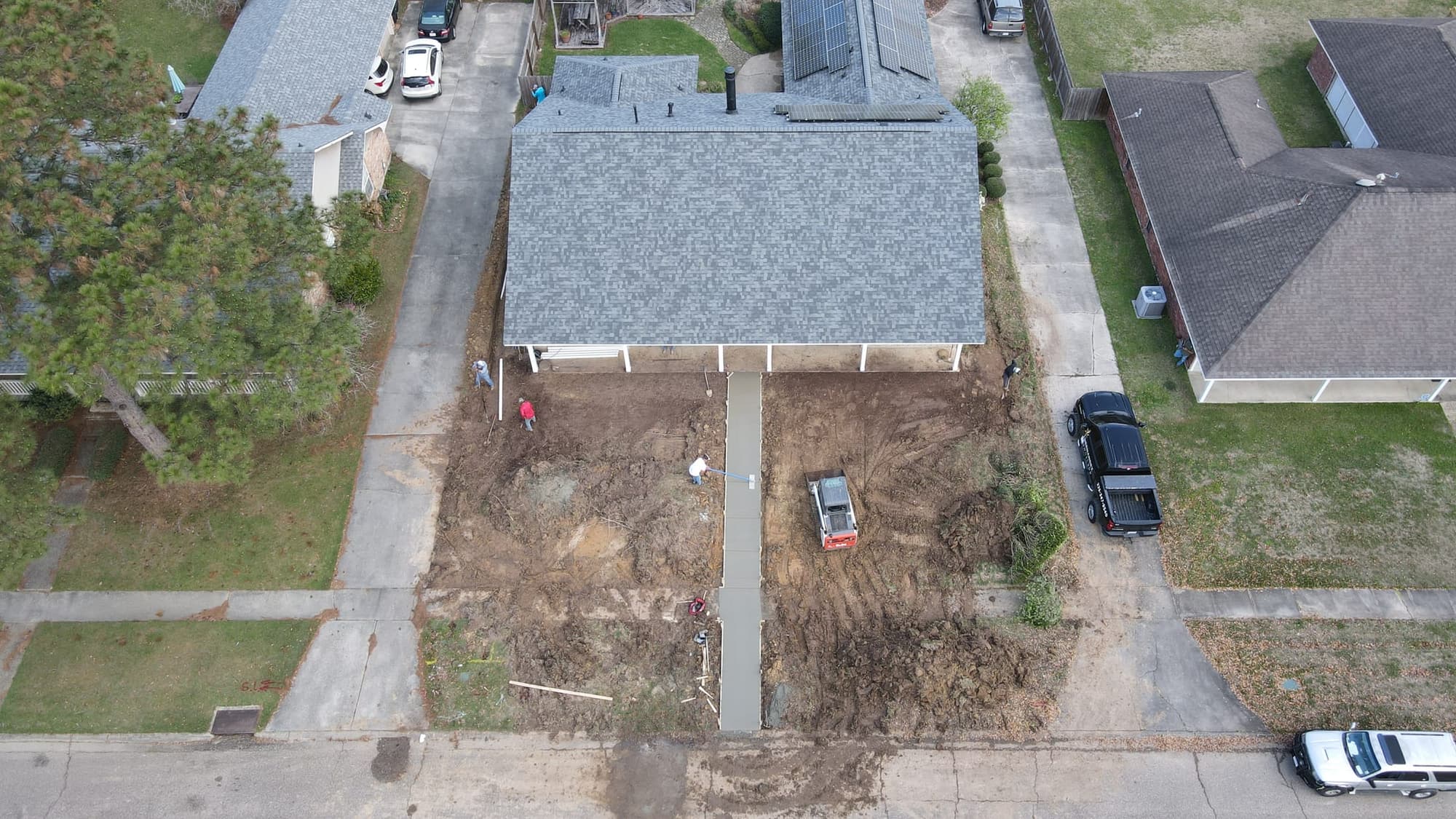 Drone view of a new concrete walkway running from the street to a home's front porch, the yard graded on both sides