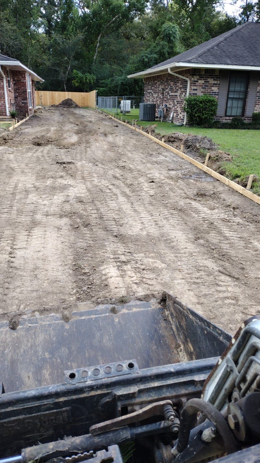 Graded lane between two homes with wood forms set along the edge, seen from the seat of the skid steer