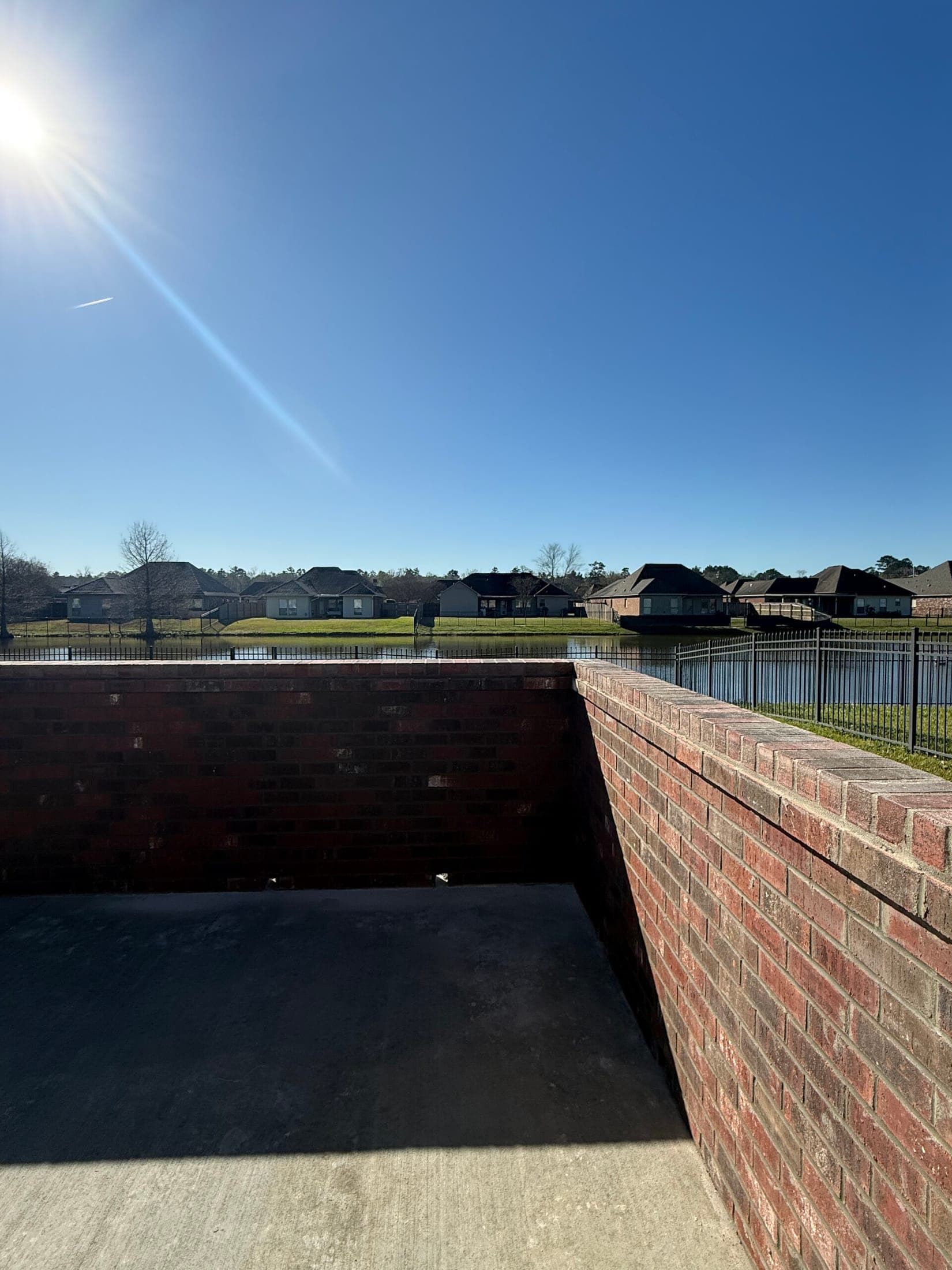 Finished concrete patio inside a brick wall overlooking a neighborhood pond