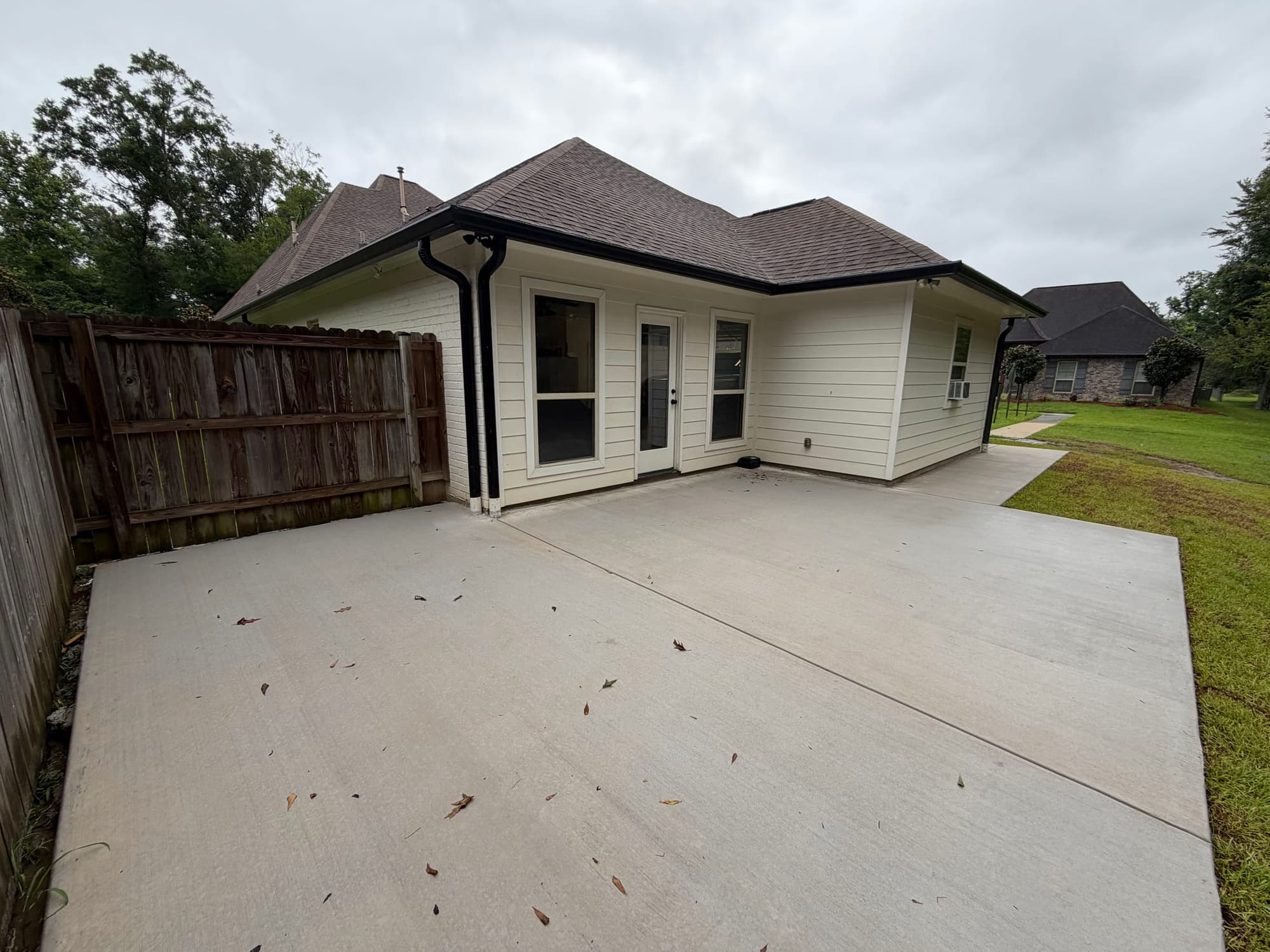 New broom-finished concrete patio across the back of a cream-sided house, wood privacy fence on the left