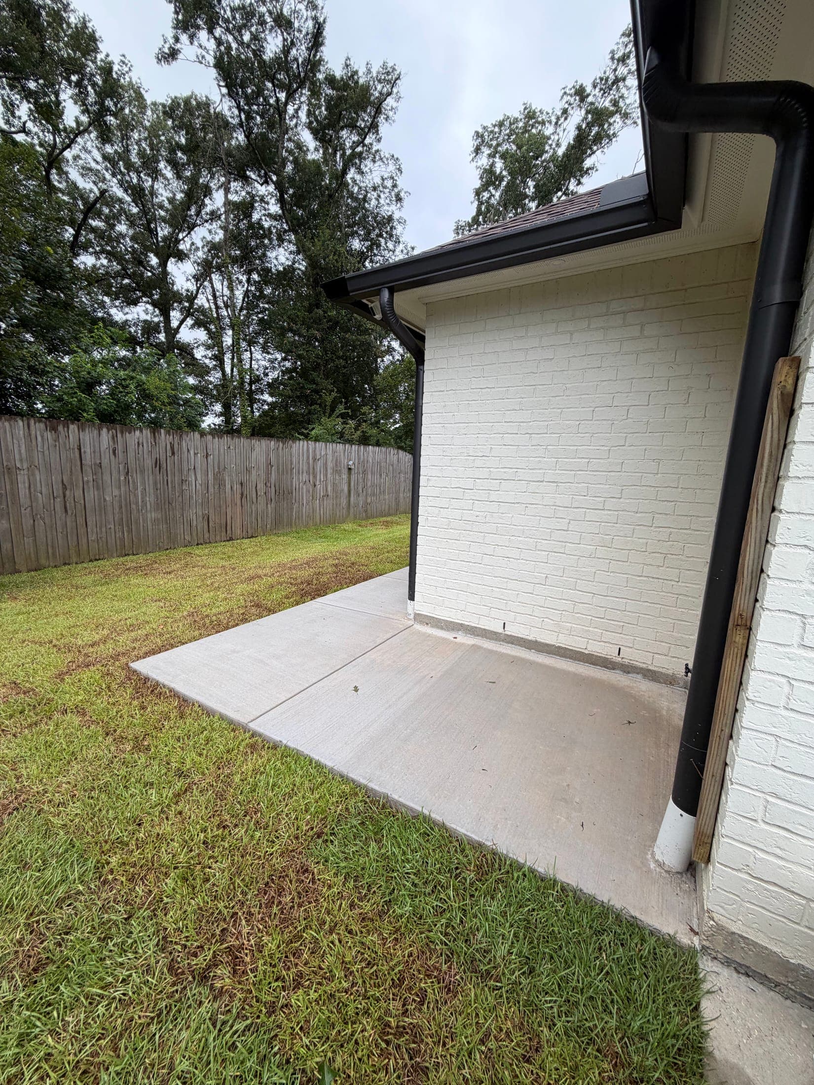 Fresh concrete slab along the side of a white-painted brick house, set below the downspout