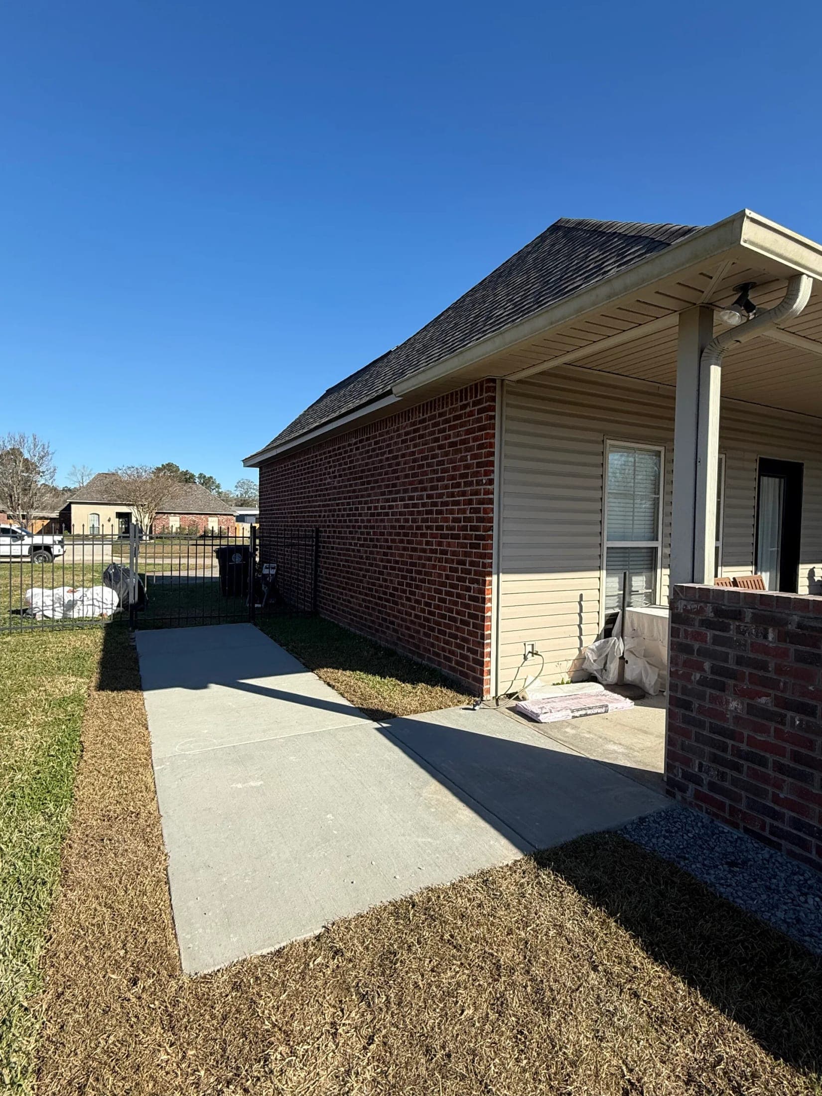 Smooth new concrete walkway along a red brick house from the iron gate to the covered patio