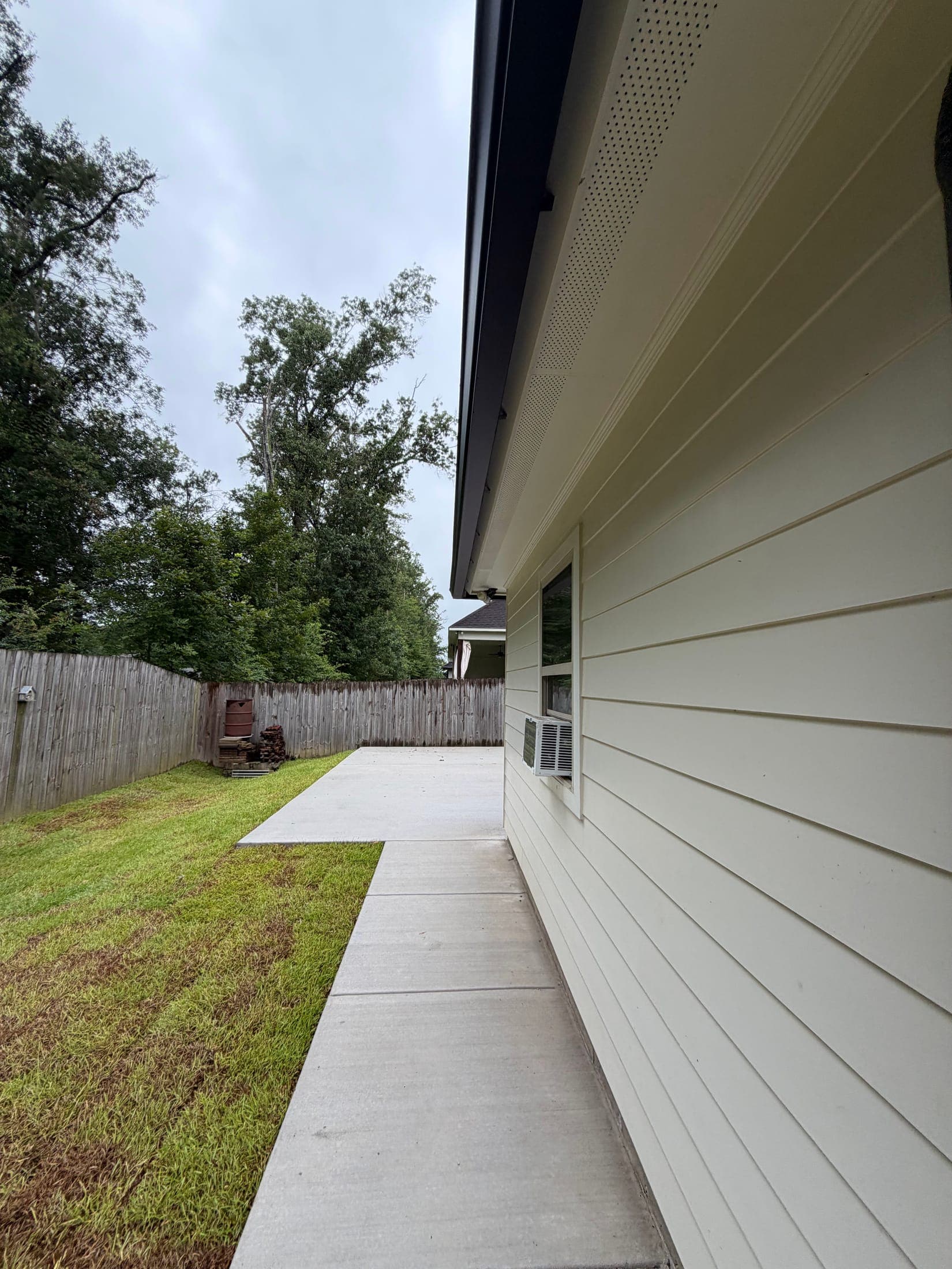 New concrete walkway running the length of a house beside the lawn and privacy fence