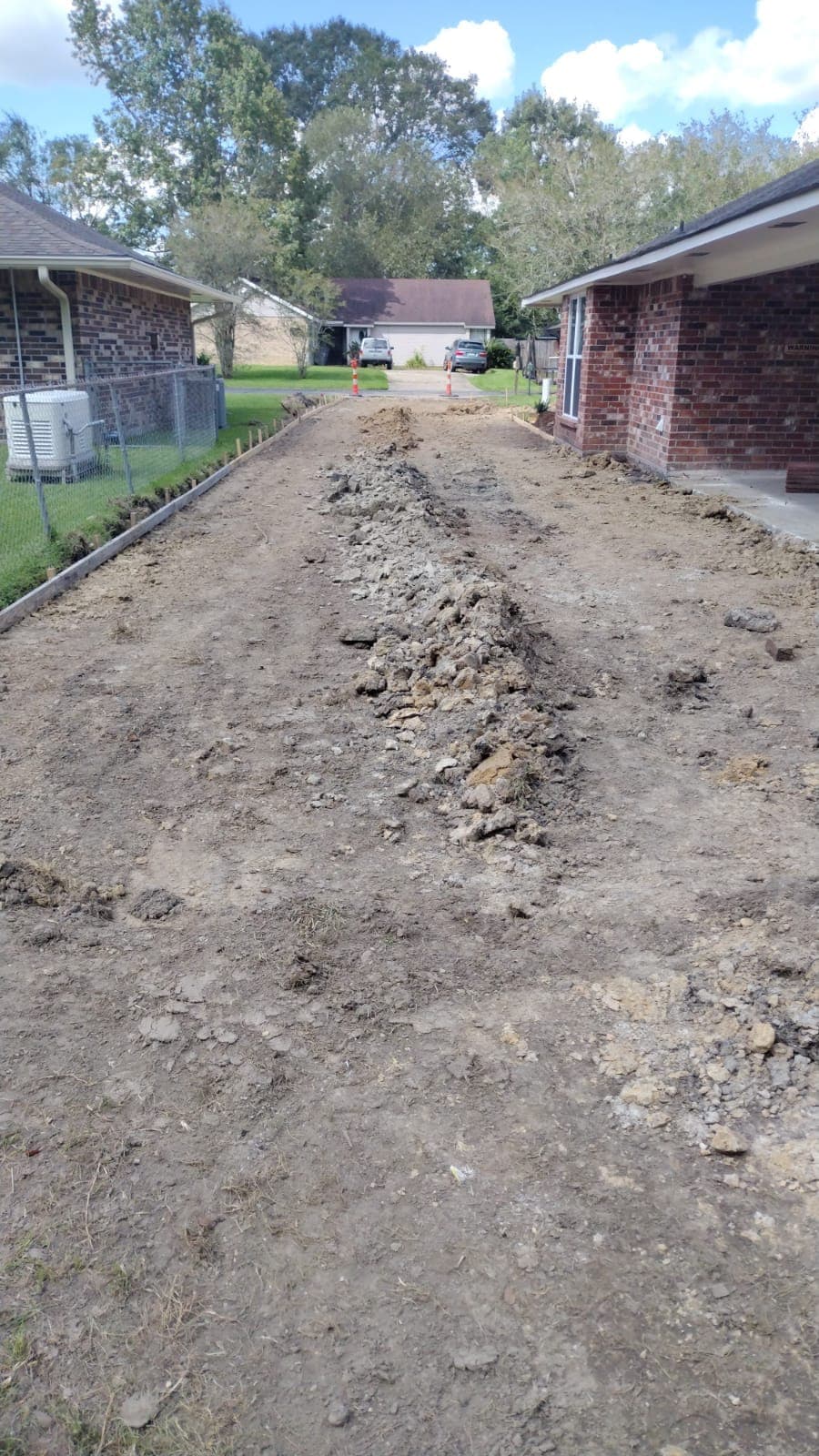 Old concrete broken out of a side yard between two brick homes, with new forms set along the edge