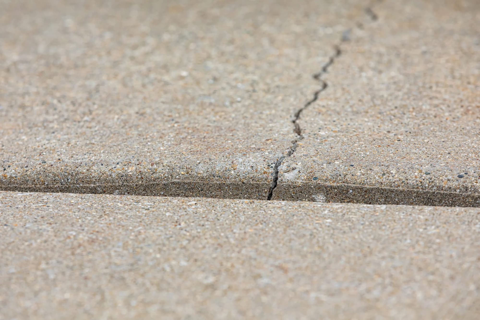 Close view of a crack running from a control joint across a concrete slab