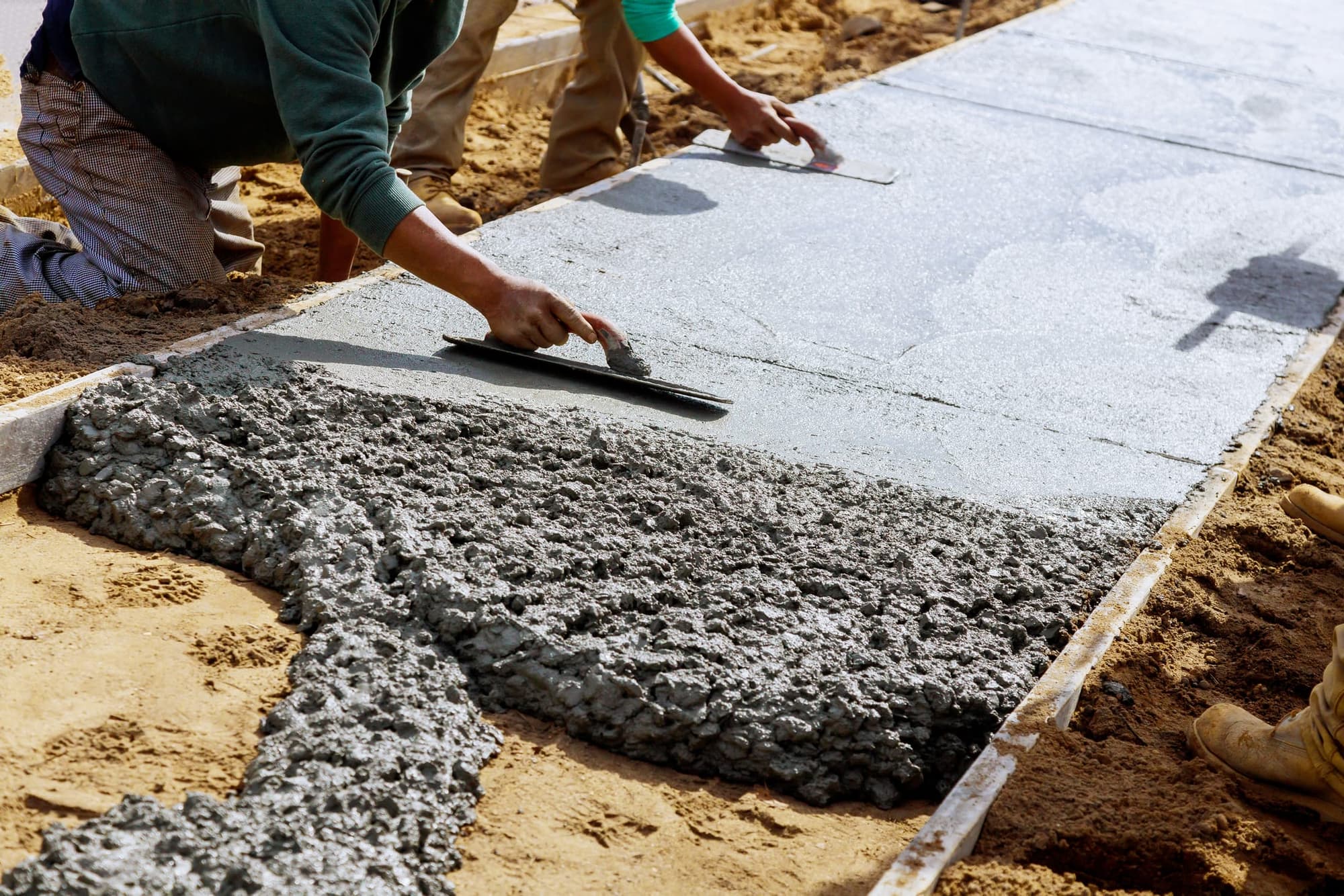 Two finishers kneeling at the form edge with hand trowels