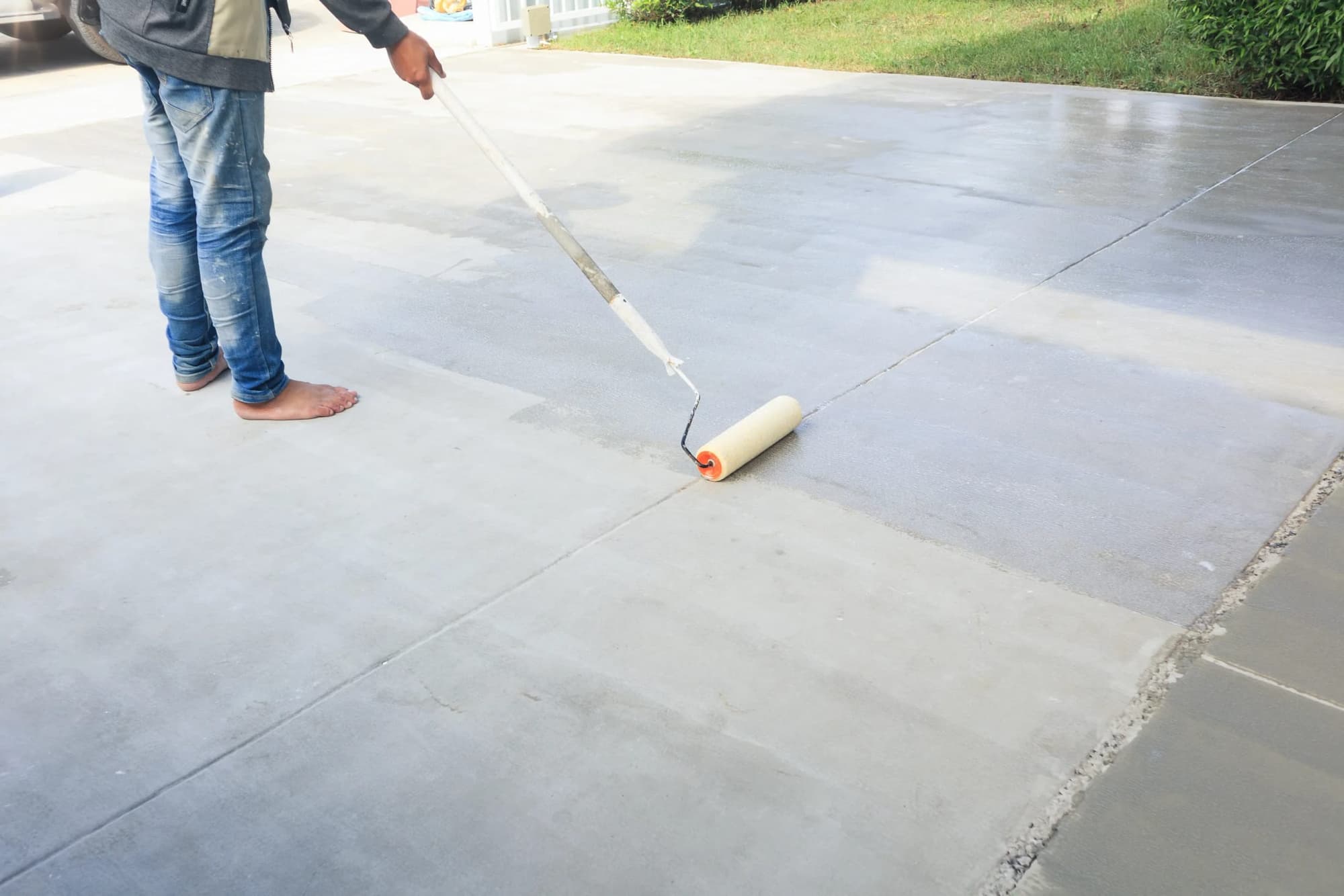 Sealer being rolled onto a concrete driveway, the treated section darker